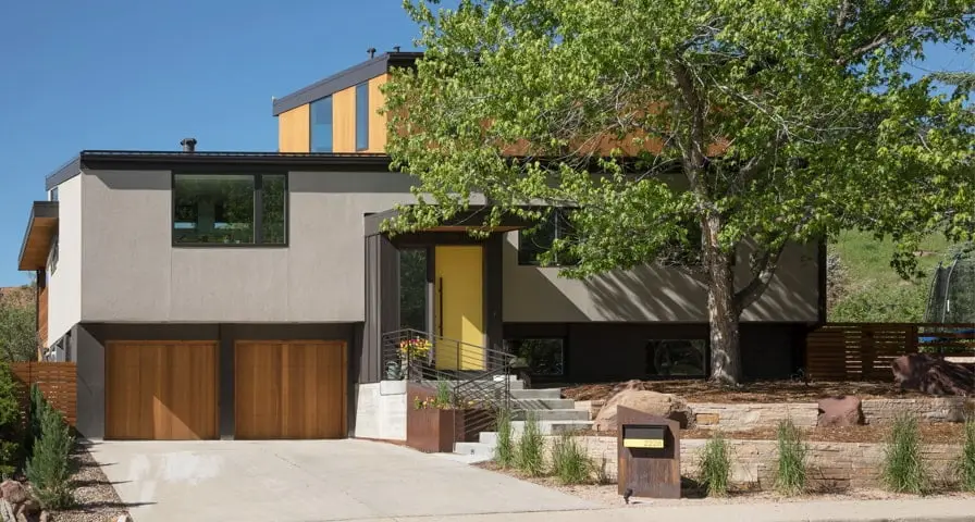 NCAR is A contemporary multi-level home with a mix of gray stucco, wood paneling, and black metal accents on its exterior front finish.